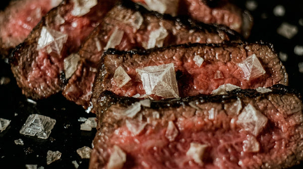 Hand streut Salz über Steak – richtiger Zeitpunkt für Finishing Salt